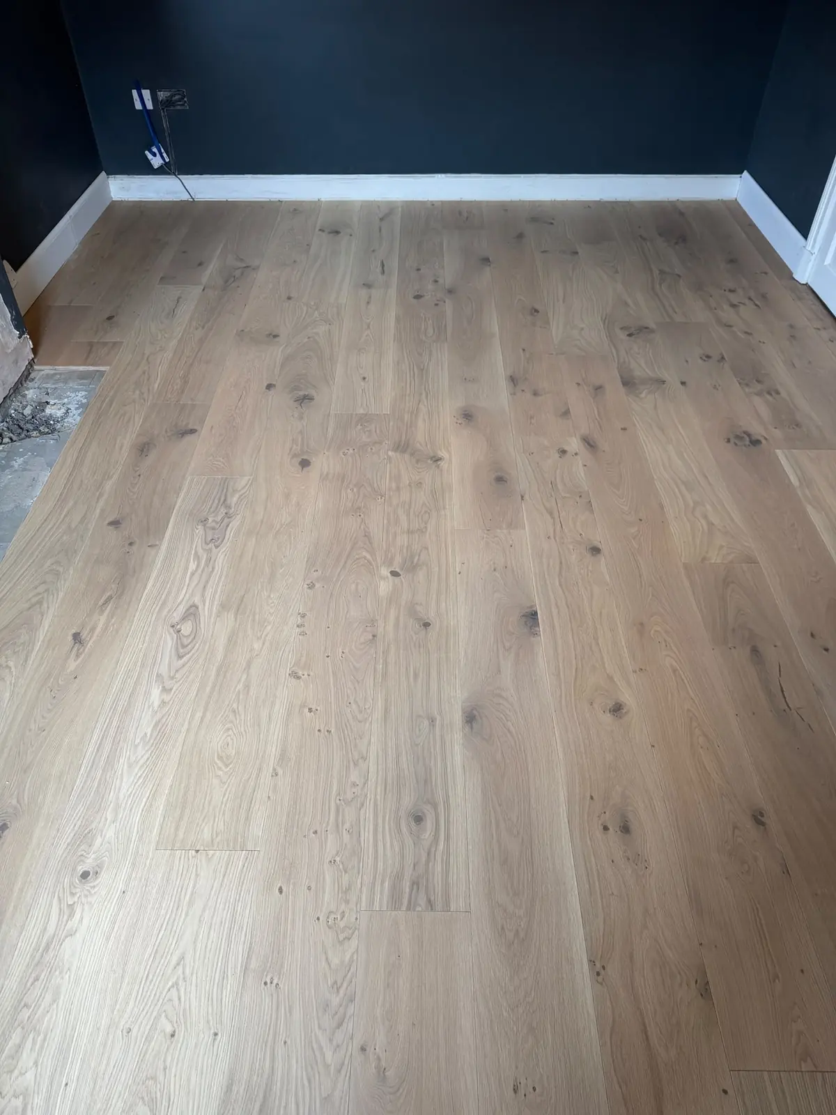Wide plank oak floor glued down to a prepared plywood subfloor, with new white ogee skirting