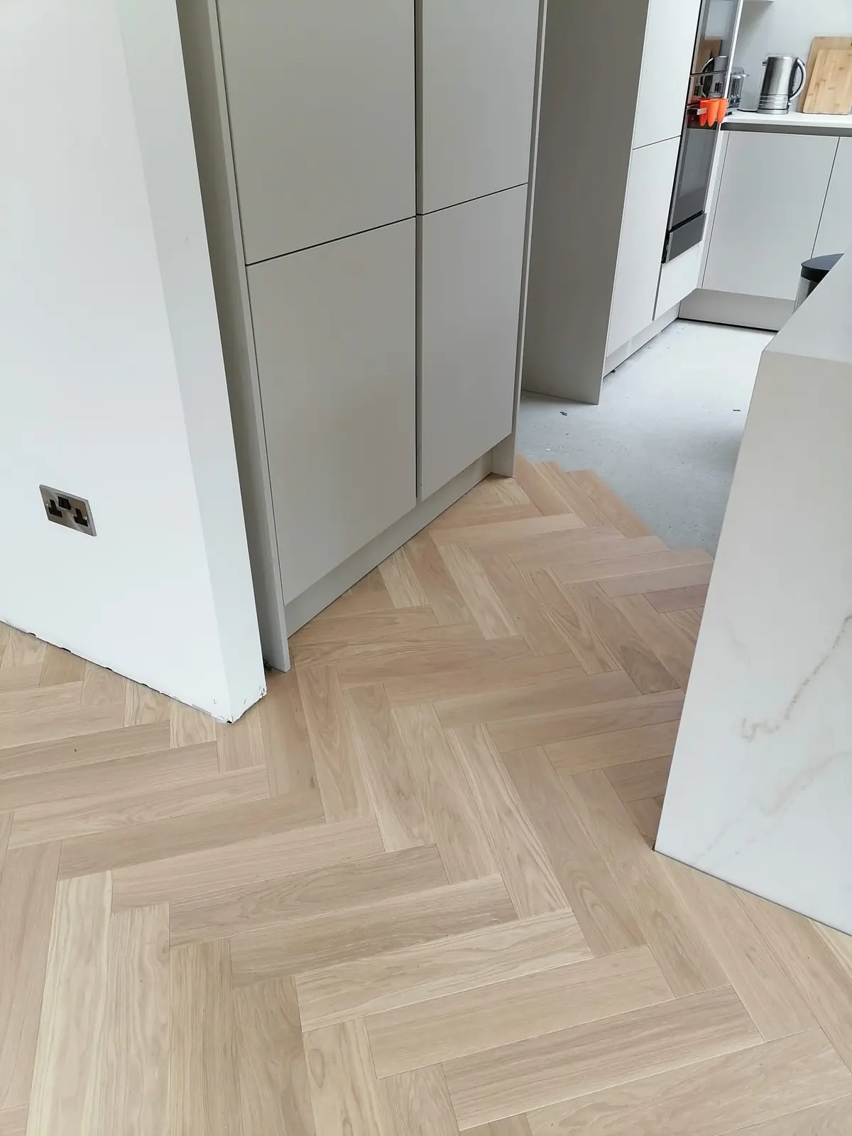 Herringbone parquet slid under the kitchen units after the kickboards were cut