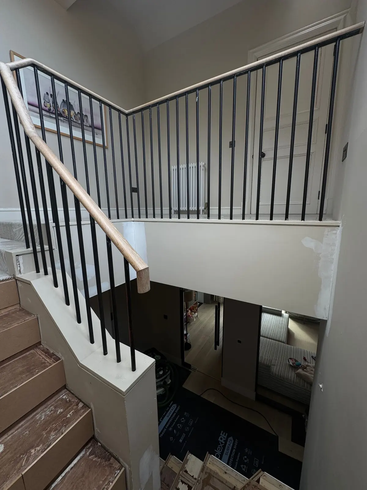 Landing and black metal balustrade before the oak stair cladding, with the old steps exposed below