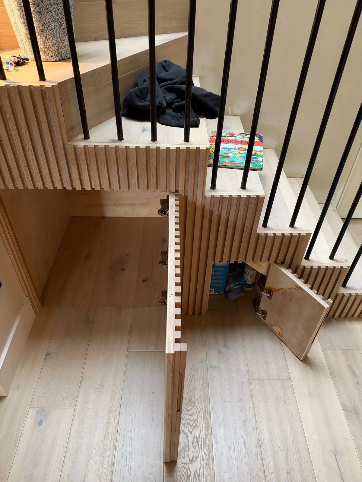 Hidden storage doors open under an oak staircase, with solid oak slat cladding