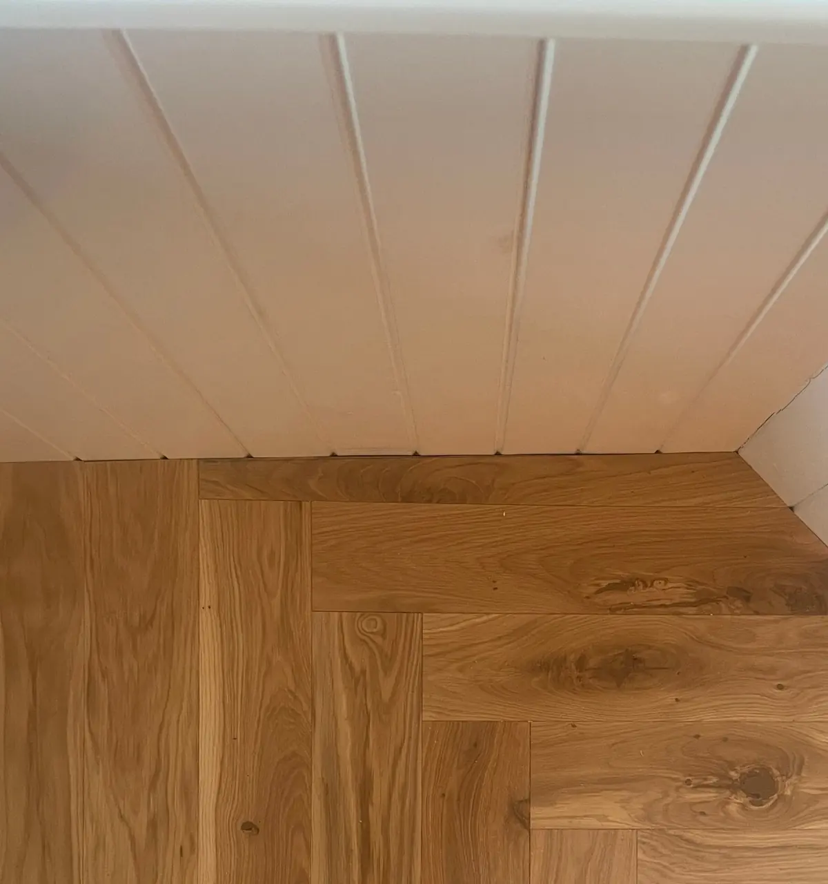 Close-up of rustic oak herringbone with knots meeting white tongue-and-groove panelling