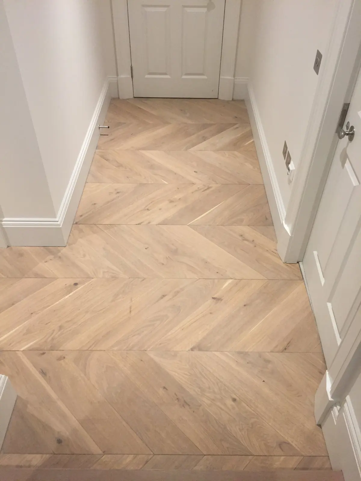 Chevron parquet hallway leading towards small steps clad in matching oak