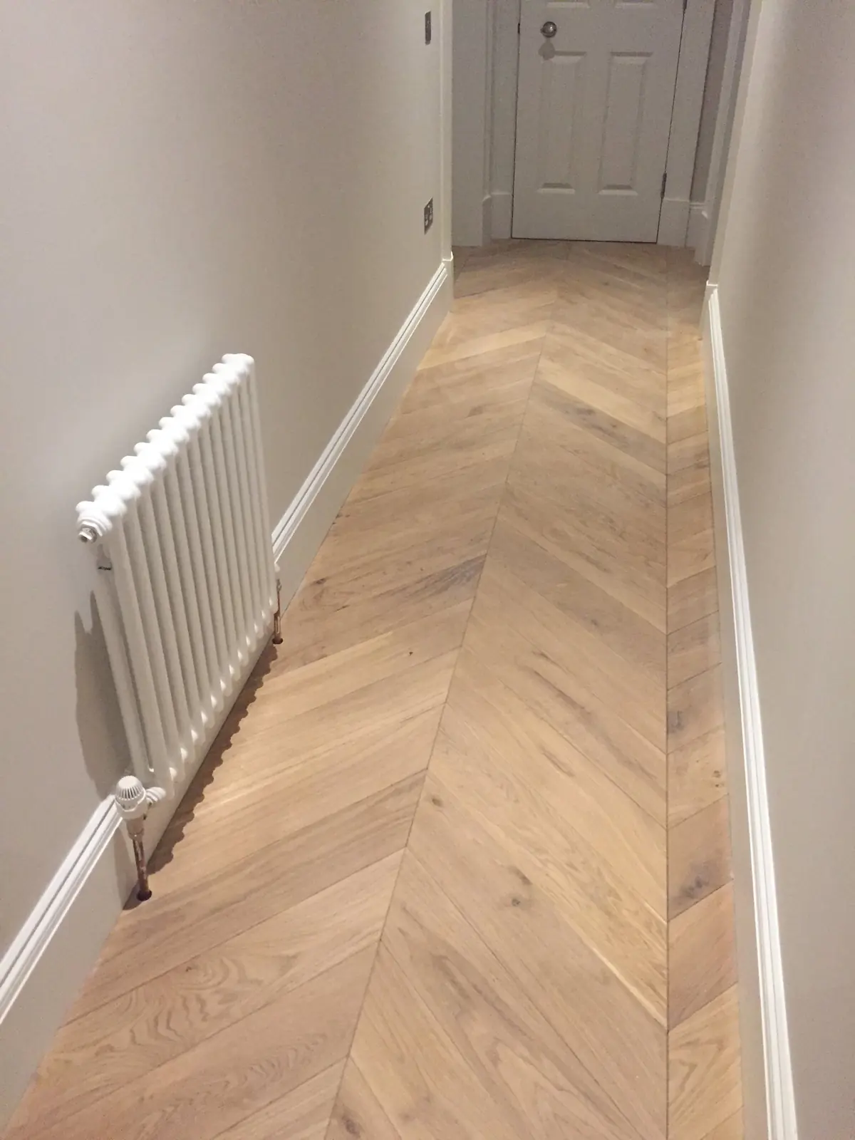 Light Oak chevron parquet in a long hallway with a radiator